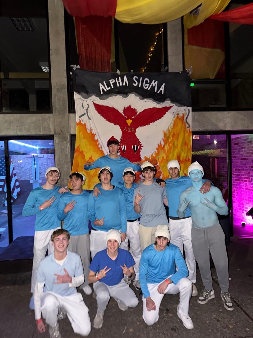Brothers in full costume in front of the Alpha Sigma Phi phoenix banner