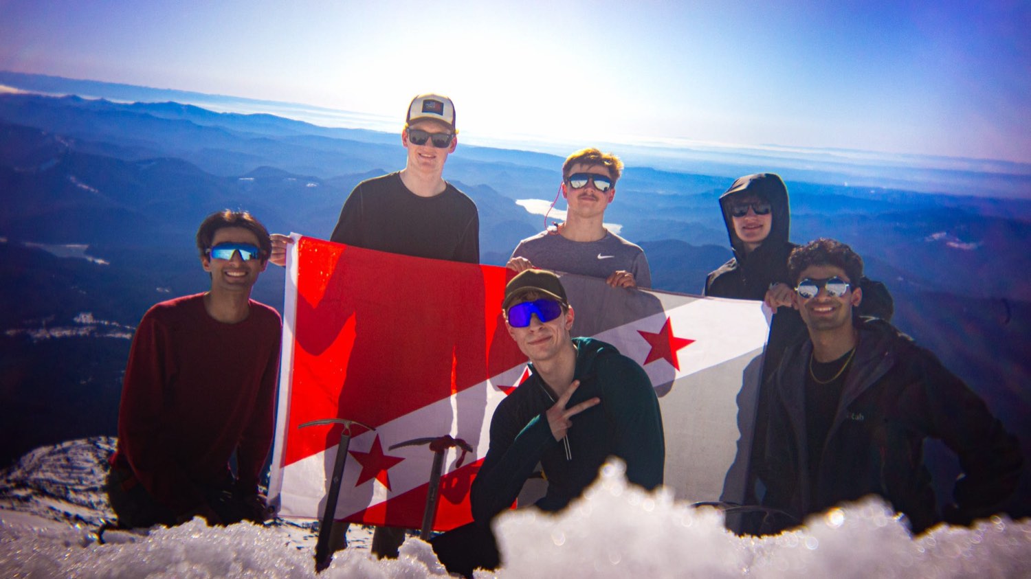 Brothers holding the Alpha Sigma Phi flag on a mountain summit above the clouds